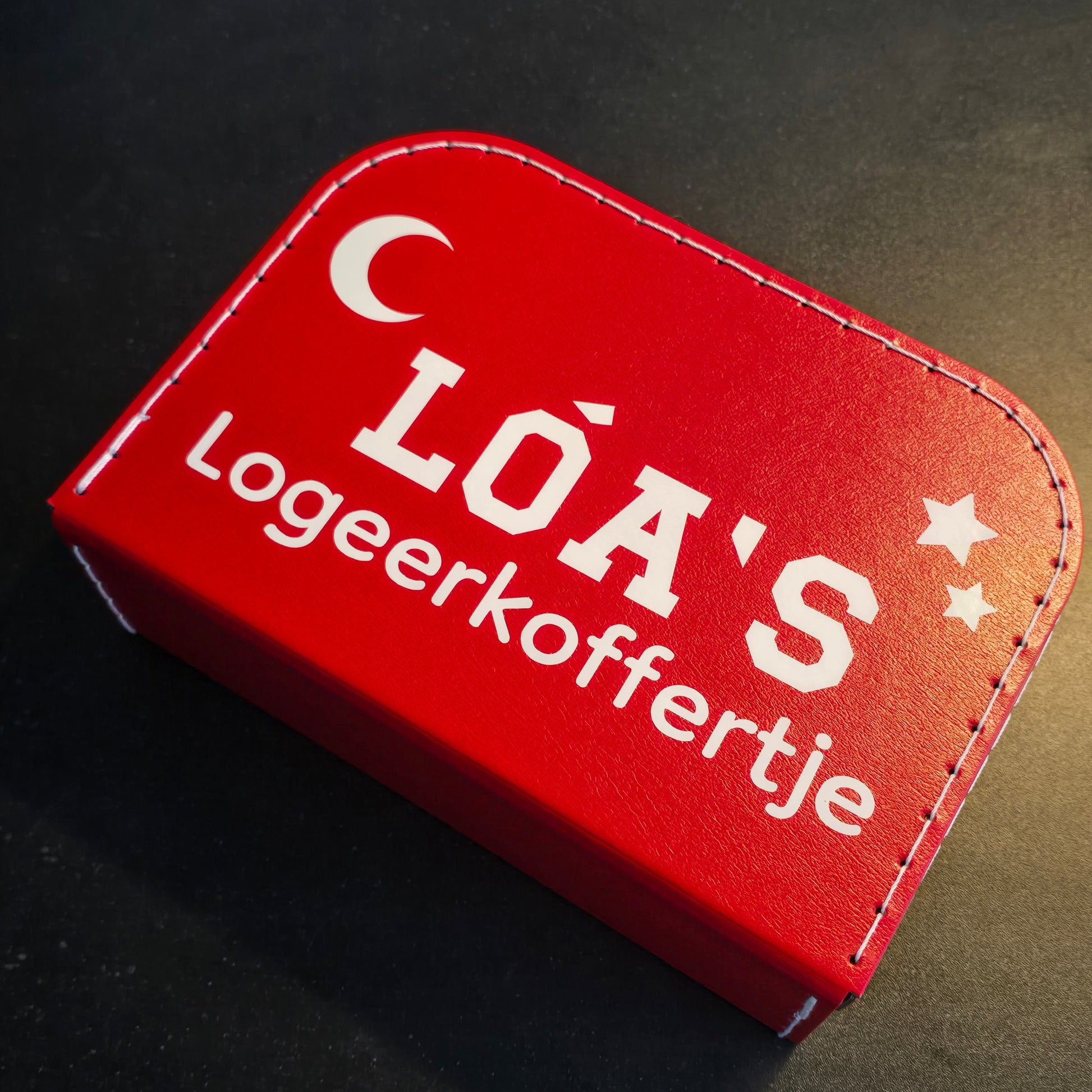 Logeerkoffer rood met bedrukking van een maan en sterren en de tekst 'Loa's logeerkoffertje'.