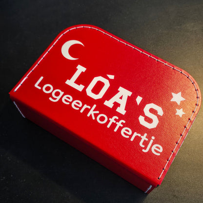 Logeerkoffer rood met bedrukking van een maan en sterren en de tekst 'Loa's logeerkoffertje'.