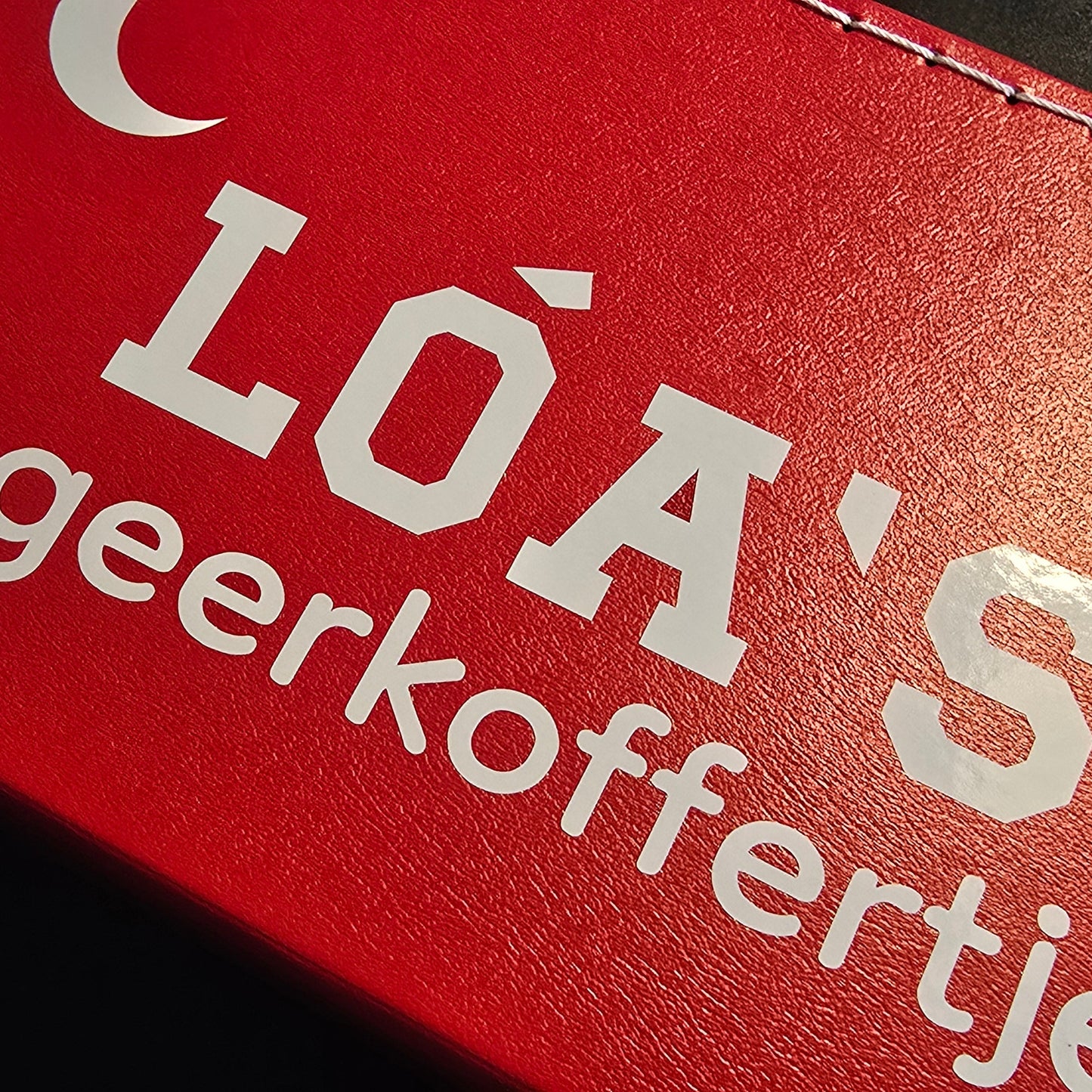 Close up van rode logeerkoffer met bedrukking 'Loa's logeerkoffertje'.